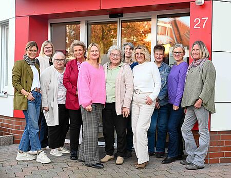 Jubiläen Vor dem Eingang des DRK-Gebäudes in Tecklenburg stehen elf Mitarbeiterinnen des Deutschen Roten Kreuzes im Tecklenburger Land eng beieinander. Sie lächeln herzlich in die Kamera – man spürt den Zusammenhalt, die Wertschätzung und den Stolz auf viele gemeinsame Jahre im Dienst der Menschlichkeit. Hinter ihnen leuchtet die rot-weiße Fassade mit der Hausnummer 27 in der Sonne. Die Szene strahlt Wärme, Nähe und Freude aus – ein Moment echter Gemeinschaft.