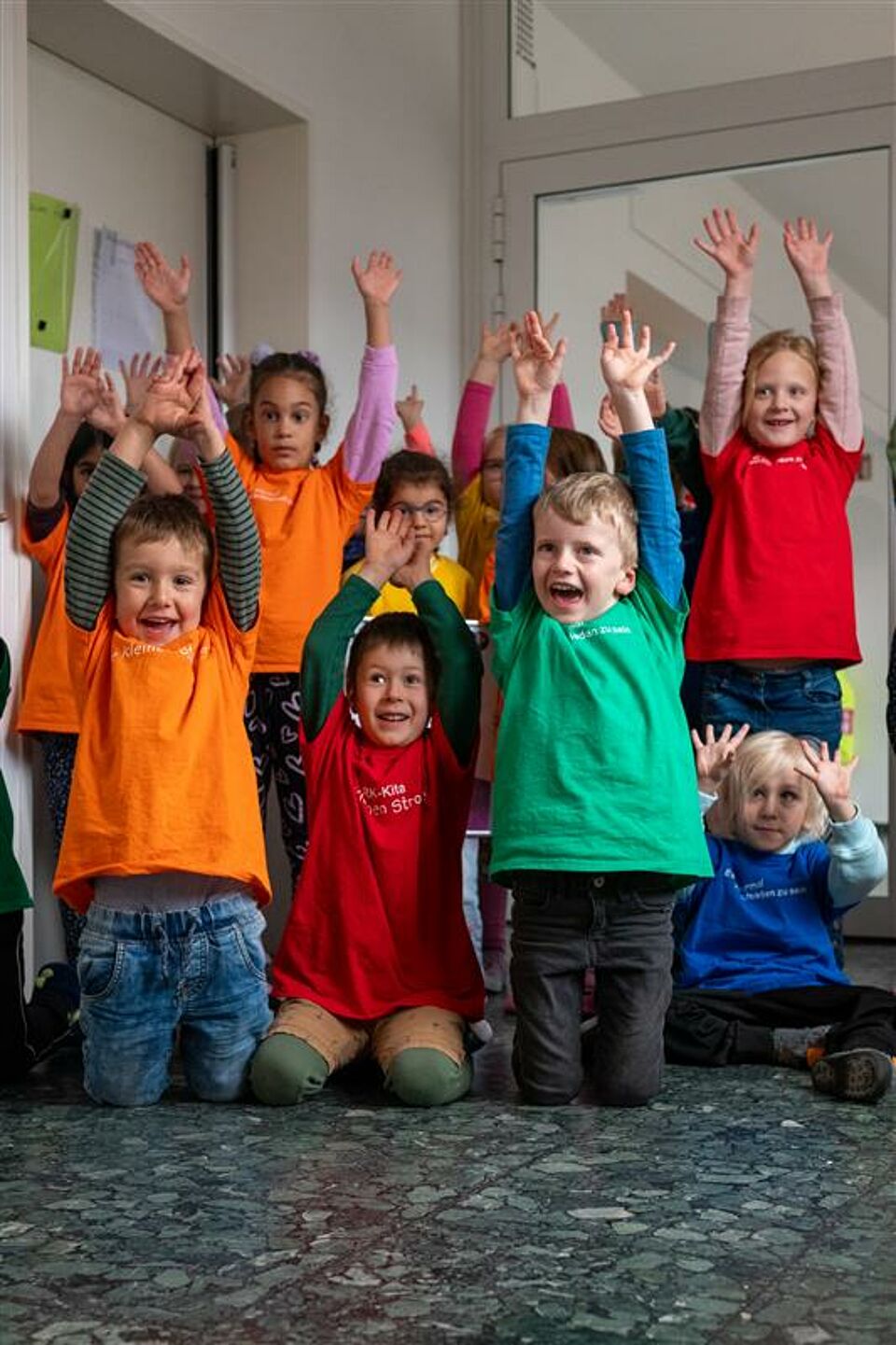 Mehrere Kinder in bunten T-Shirts heben lachend die Arme hoch.
