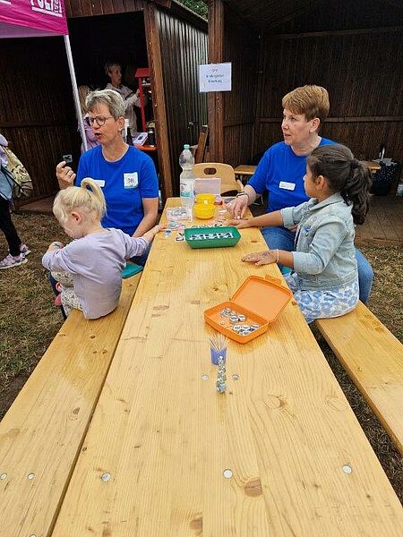 Zwei Frauen in blauen T-Shirts sitzen mit zwei Kindern an einem Holztisch und beschäftigen sich mit Schraubenmuttern beim Altstadtfest Bevergern.