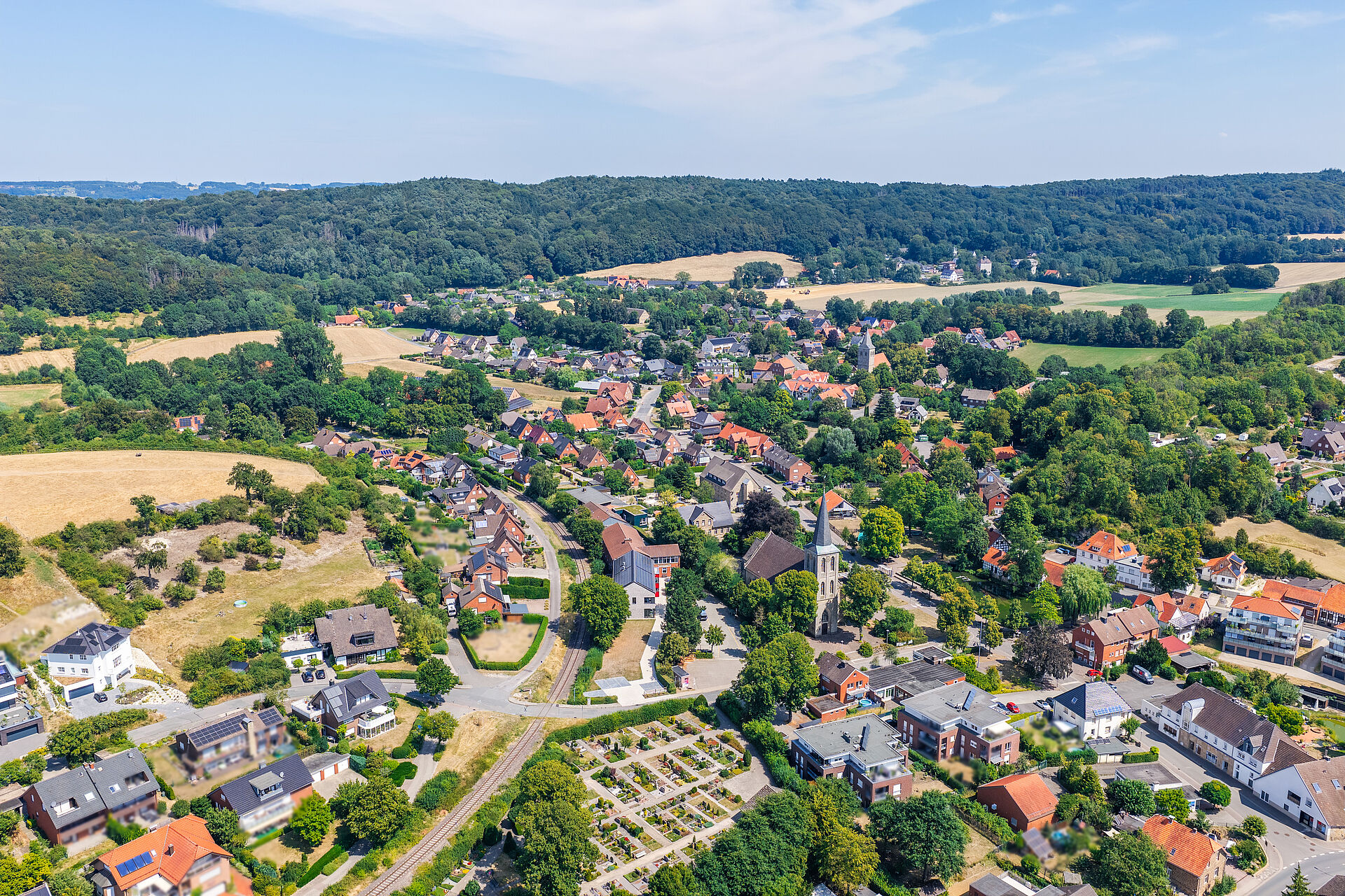 Brochterbeck im Tecklenburger Land Luftaufnahme des Ortes Brochterbeck: Das Dorf mit seinen rot gedeckten Häusern liegt eingebettet in grüne Felder und Wälder; im Zentrum hebt sich die Kirche mit ihrem hohen Turm ab, im Hintergrund bewaldete Hügel.