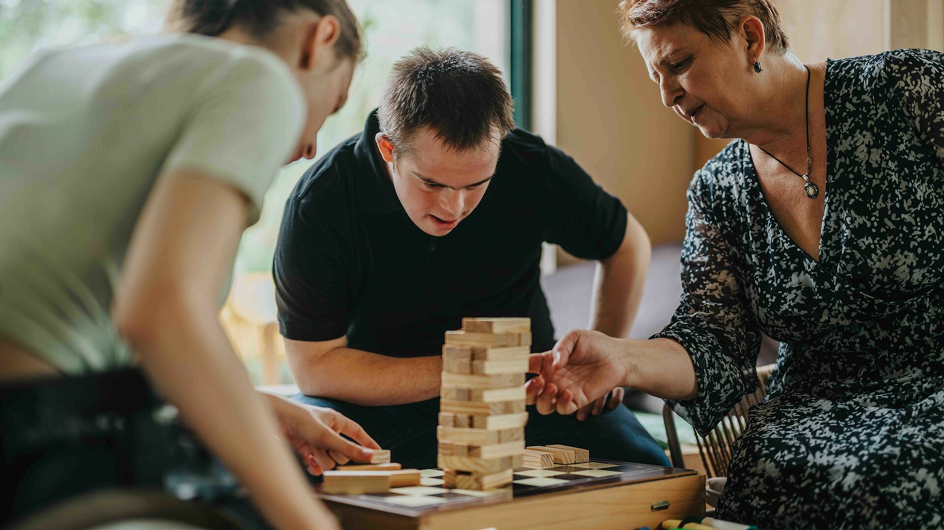 Drei Personen sitzen um einen Tisch und spielen gemeinsam Jenga.