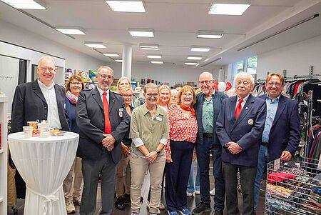 Eröffnung Kleidershop_1.10.2026 Elf lächelnde Personen stehen in einer Reihe im hell beleuchteten Kleidershop mit Kleidungsständern und Regalen.